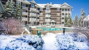 Een meerlaags hotel met balkons, een zwembad en een besneeuwde omgeving.