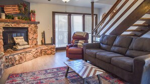 A living room with a fireplace, a sofa, a chair, a patterned rug, and a staircase. - Mountain/River Rider at Brookside (Red River)