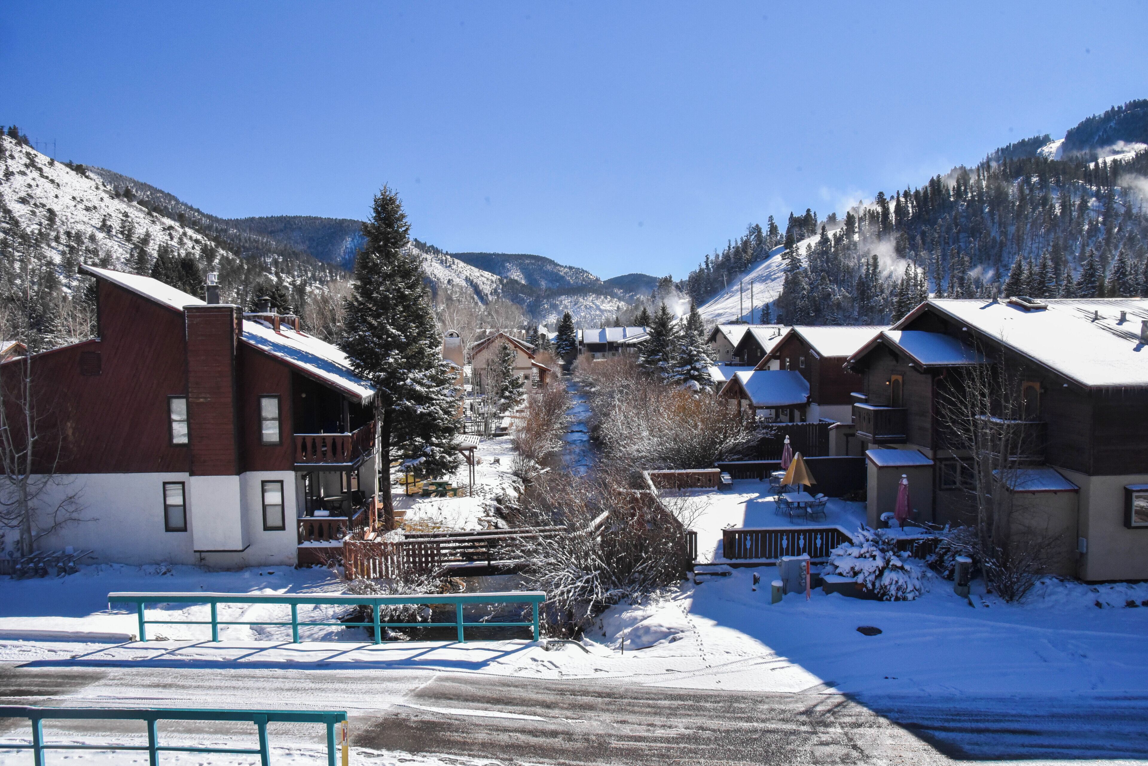 Un village de montagne enneigé, avec des bâtiments de style chalet, un télésiège et un ciel bleu dégagé.