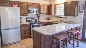 A kitchen with wooden cabinets, a refrigerator, a stove, and a marble island with bar stools. - Mountain/River Rider at Brookside (Red River)