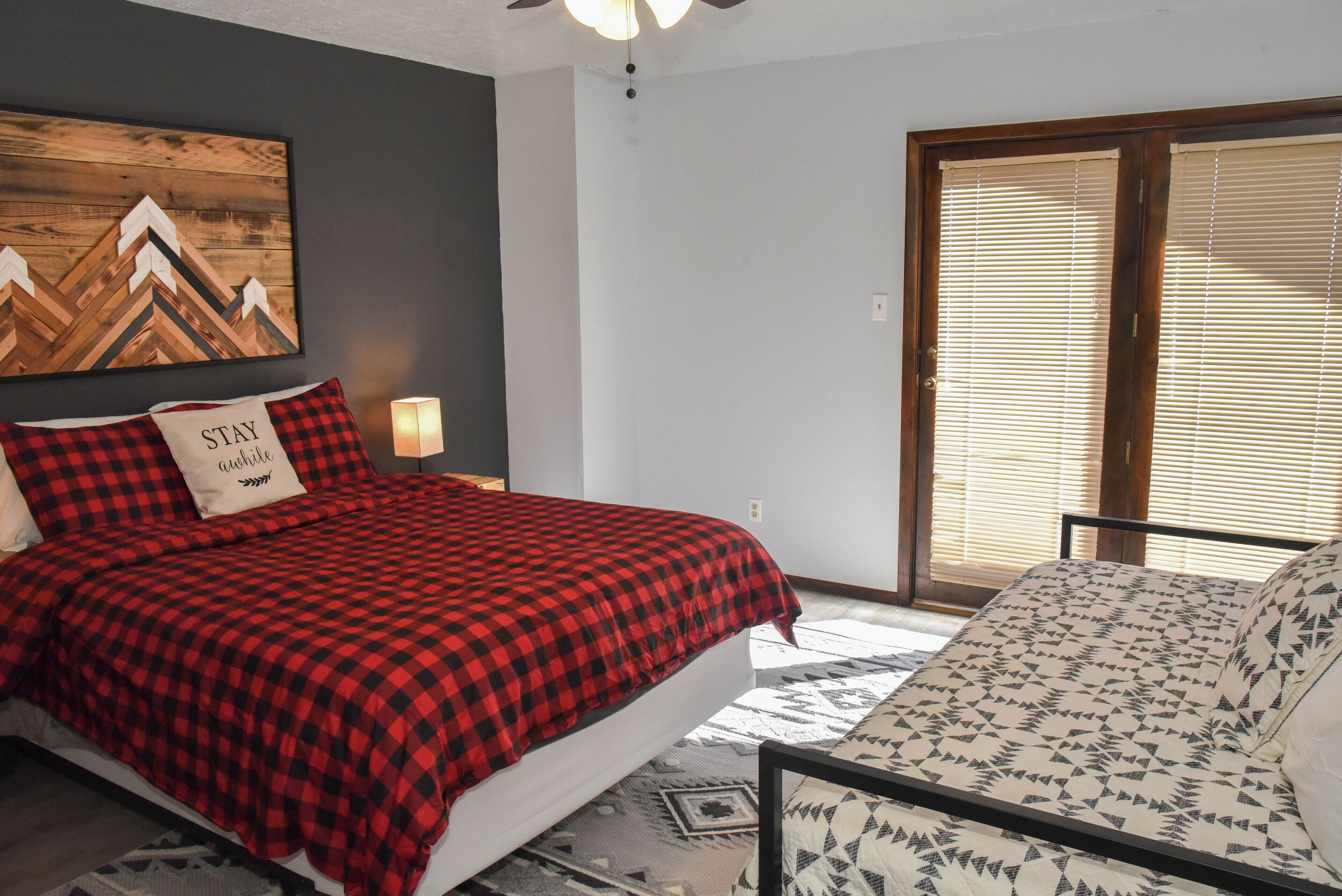 Een slaapkamer met een bed, een kussen met de tekst 'STAY', een wanddecoratie en een raam met zonwering.