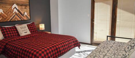 Een slaapkamer met een bed, een kussen met de tekst 'STAY', een wanddecoratie en een raam met zonwering.