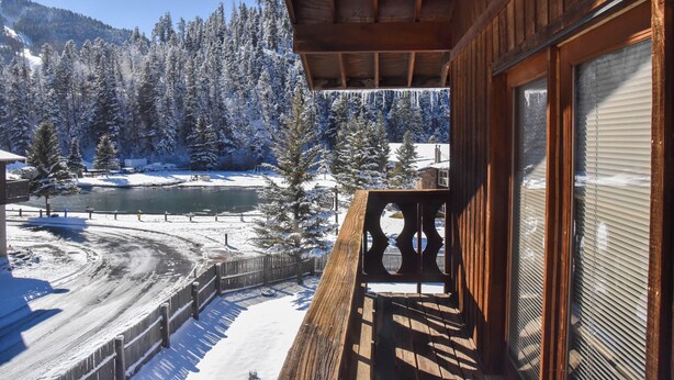 A wooden cabin with a balcony overlooking a snowy landscape and a river. - Mountain/River Rider at Brookside (Red River)