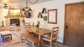 A dining area with a wooden table, benches, and chairs, a fireplace, and a stone wall. - Mountain/River Rider at Brookside (Red River)