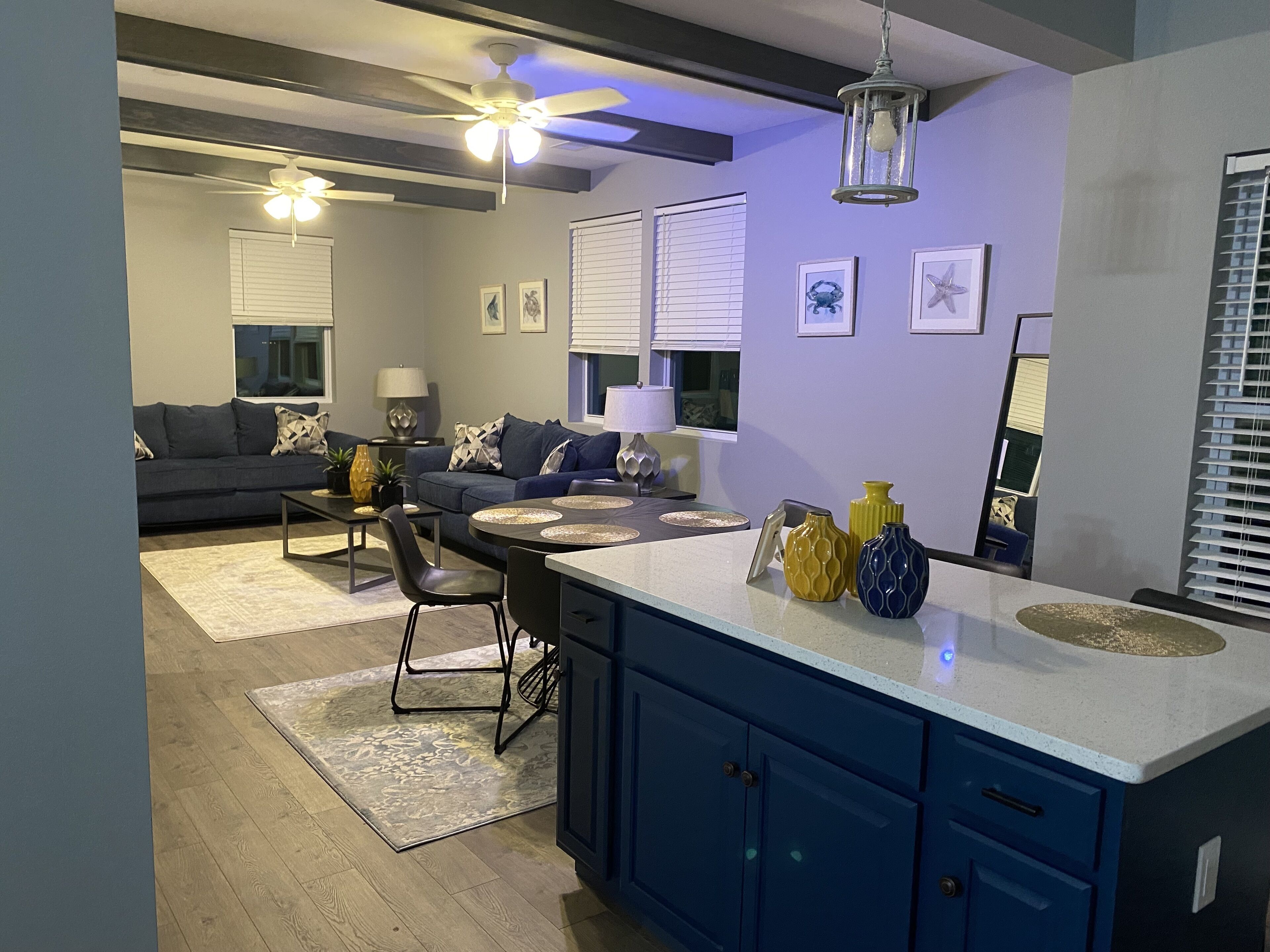 A modern kitchen with blue cabinets, a white countertop, and a dining area with a black chair and table.