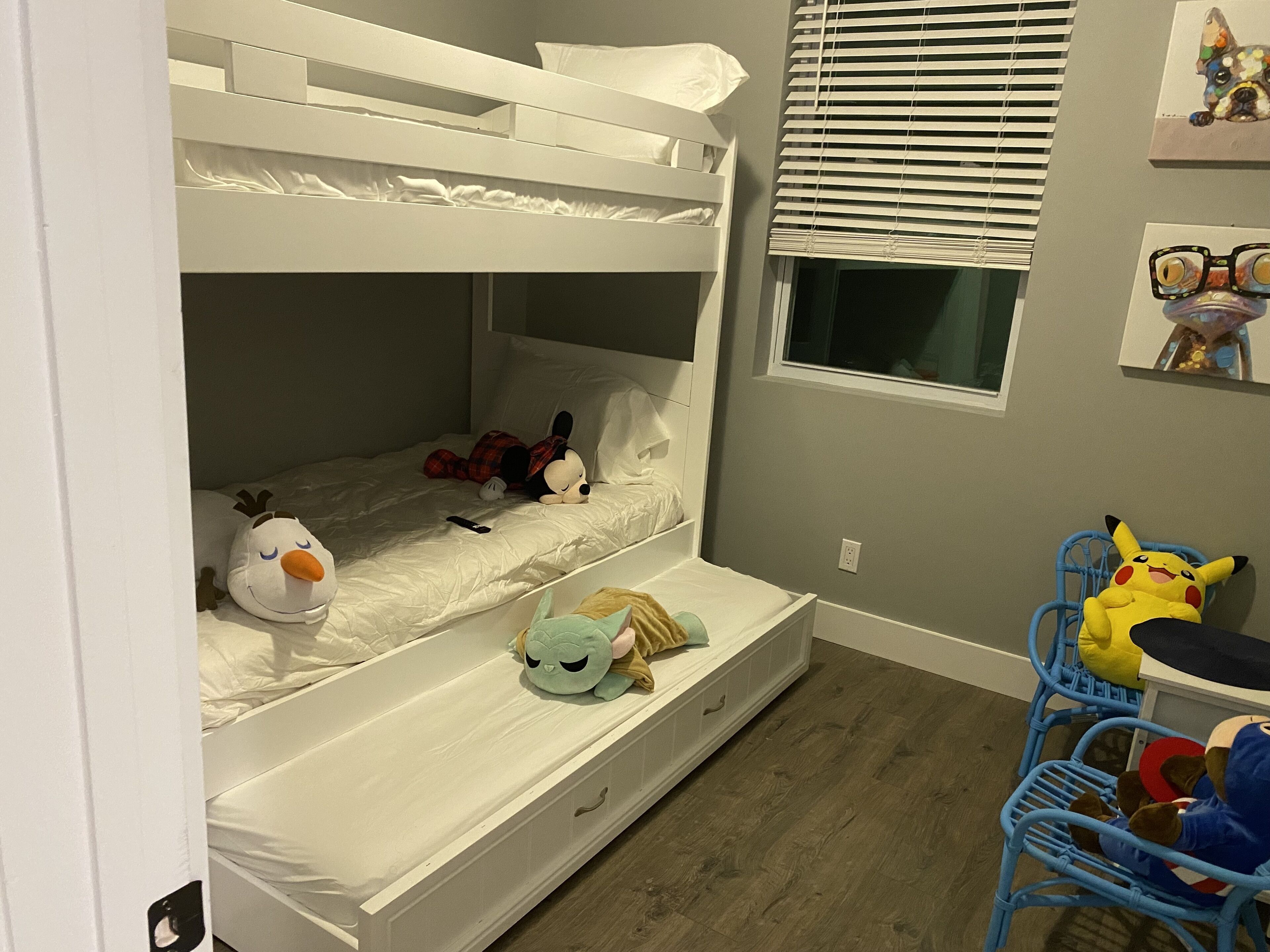 A bunk bed with plush toys, a window with blinds, and a small table with chairs.