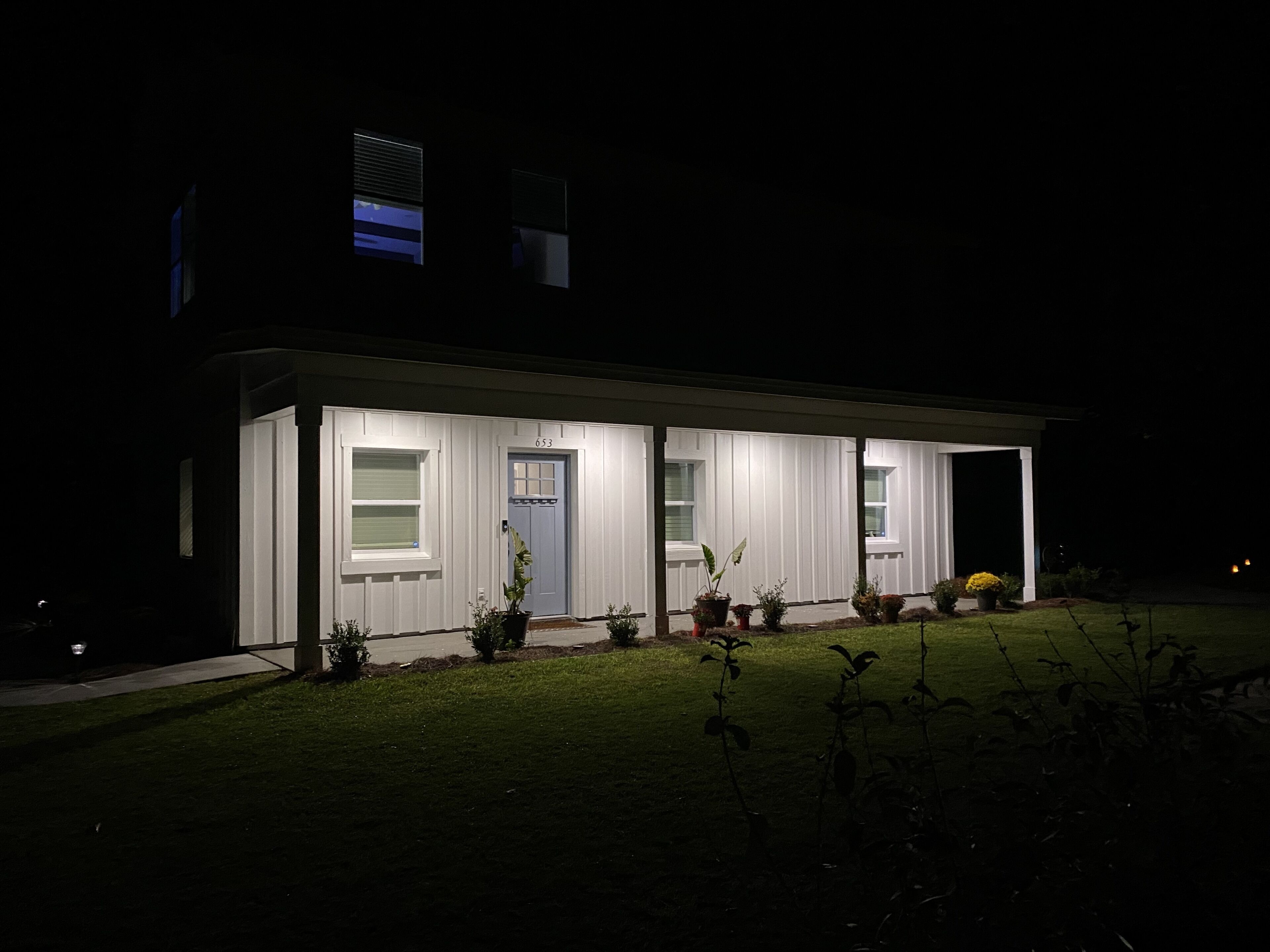 Een modern huis met een blauwe deur, een witte gevel en een goed verlichte veranda.