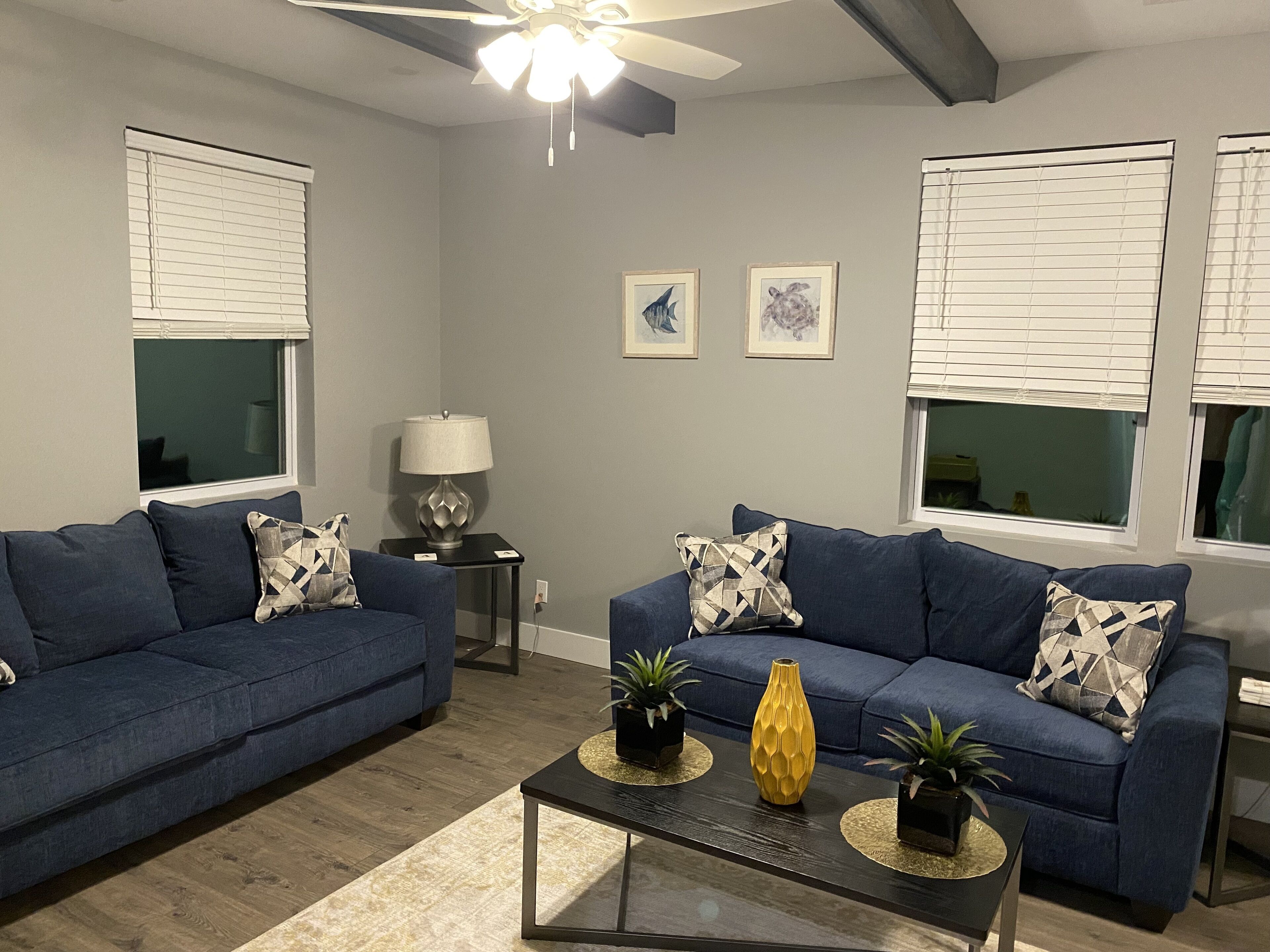 A living room with two blue sofas, a coffee table, a lamp, and two framed pictures on the wall.
