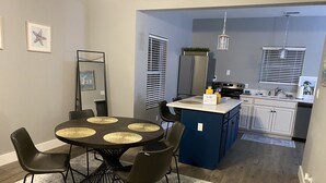 Une cuisine compacte dotée d’un îlot central, d’un coin repas avec une table ronde et des chaises, et d’un petit îlot avec un évier.
