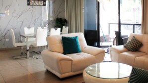 Ein modernes Wohnzimmer mit einem beigefarbenen Sofa, einem Glastisch und weißen Stühlen.