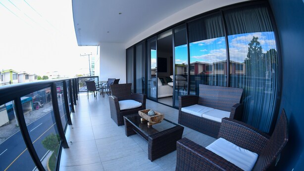 Ein moderner Balkon mit Korbmöbeln, einem Glastisch und Blick auf die Stadtlandschaft.