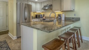 A modern kitchen with a central island, stainless steel appliances, and wooden bar stools. - First Floor Ocean View! Pet Friendly! Sleeps 6! Amenity access included! (Seabrook Island)