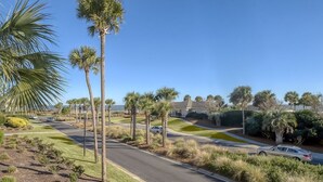 A residential street lined with palm trees and houses, with a clear blue sky. - First Floor Ocean View! Pet Friendly! Sleeps 6! Amenity access included! (Seabrook Island)