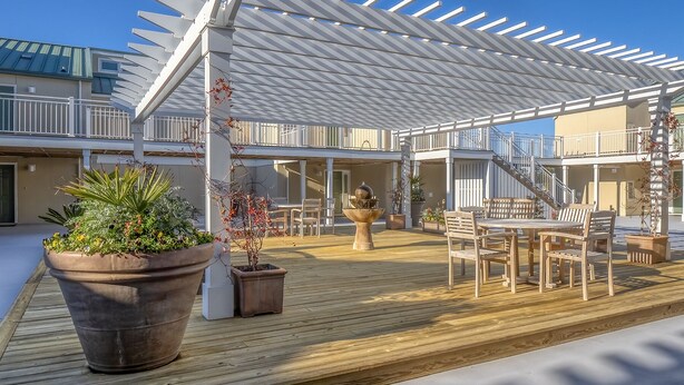 A covered outdoor area with a wooden deck, potted plants, and a seating arrangement. - First Floor Ocean View! Pet Friendly! Sleeps 6! Amenity access included! (Seabrook Island)