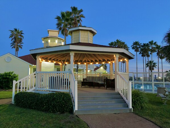 A gazebo with a covered patio, steps leading up to it, and a pool in the background.