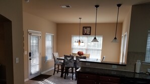 Una cocina con zona de comedor, que incluye una isla central, lámparas colgantes y un ventanal con persianas.