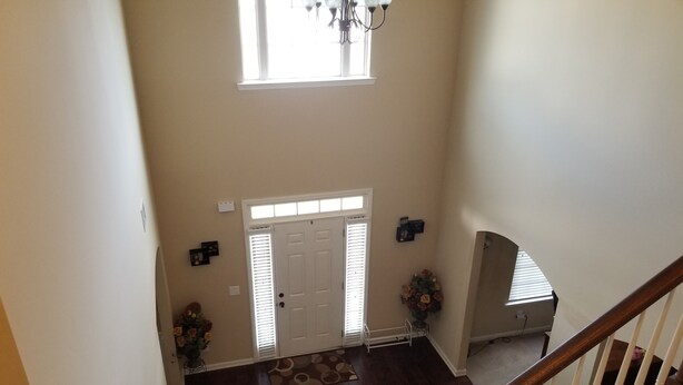 Un interior espacioso con una escalera de madera, una puerta blanca y un candelabro.