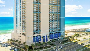 Un hotel di grandi dimensioni con numerosi balconi, vista sulla spiaggia e un'area di parcheggio con palme.