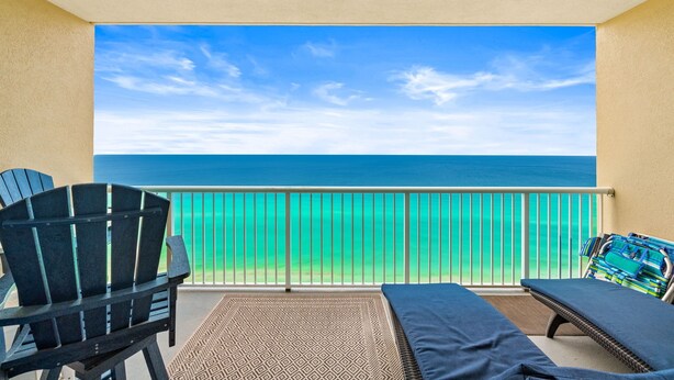 Un balcone con vista sull'oceano, una sedia, una poltrona prendisole e un tappeto decorato.