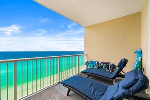 A balcony with two lounge chairs, a patterned rug, and a view of the ocean.