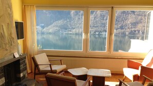 A living room with a fireplace, a television, and a view of a lake.