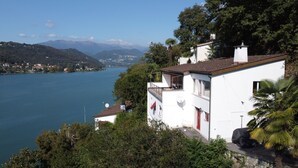 A white building with a balcony overlooking a lake and mountains.