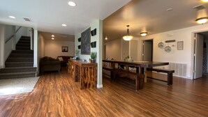 A spacious living area with a wooden floor, a dining table with benches, a staircase, and a large window.