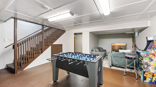 A spacious room with a foosball table, a sofa, and a gaming console.