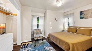 A bedroom with a bed, a chair, a desk, and a window with curtains.