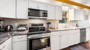 A modern kitchen with white cabinets, a stainless steel stove, a microwave, and a dishwasher.