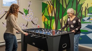 Dues persones jugant a futbolí en una habitació amb decoració mural colorida.