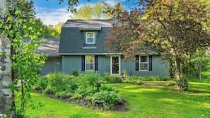 A two-story house with a front porch, a small garden, and a tree to the right.