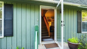 Uma casa com fachada verde, escadaria visível para um andar superior, e porta aberta para o interior.