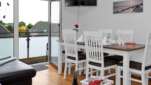 A modern living room with a dining area, a flat-screen TV mounted on the wall, and a view of the outdoors. - Apartment Sturm by Interhome (Warwerort)