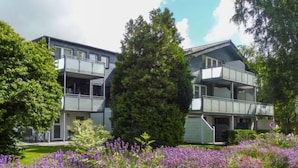 A modern two-story building with balconies, surrounded by lush greenery and purple flowers. - Apartment Sturm by Interhome (Warwerort)