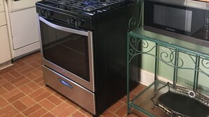 Et køkken med gasblus, ovn, mikrobølgeovn og en grøn metalkasse med køkkenudstyr.