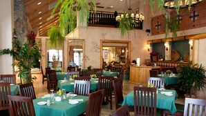 Ein Restaurant mit Holztischen und -stühlen, grünen Tischdecken und hängenden Pflanzen.