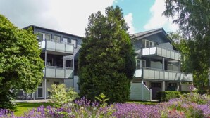 A modern two-story building with balconies, surrounded by lush greenery and purple flowers. - Apartment Fasan by Interhome (Warwerort)