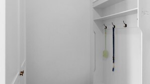 A white room with a door, a white shelf, and three hooks with items hanging on them. - Apartment Fasan by Interhome (Warwerort)