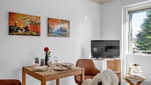 A modern living room with a wooden dining table set for two, a comfortable sofa, and a television on a stand. - Apartment Fasan by Interhome (Warwerort)
