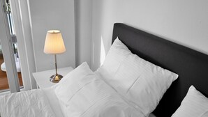 A neatly made bed with white bedding and a black headboard, accompanied by a bedside lamp on a white nightstand. - Apartment Fasan by Interhome (Warwerort)