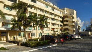 A multi-story hotel with a row of parked cars in front. - Cozy Studio In Beachfront Condominium (Cancun)