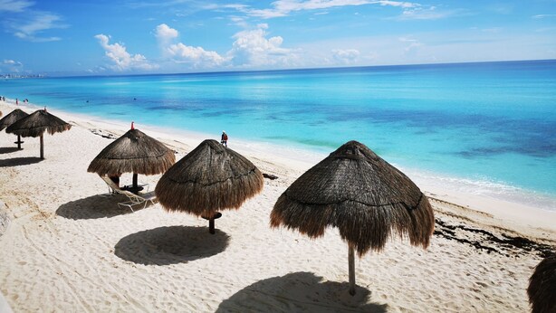 A beach with thatched umbrellas and a clear blue ocean. - Cozy Studio In Beachfront Condominium (Cancun)