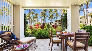 A covered patio with a table set for breakfast, lounge chairs, and a view of palm trees and greenery. - Turtle Bay Villas 108 by Gather w/ Shared Pool, Spa, AC (Kahuku)