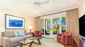 A living room with a sofa, armchairs, a coffee table, a TV, and a ceiling fan. - Turtle Bay Villas 108 by Gather w/ Shared Pool, Spa, AC (Kahuku)