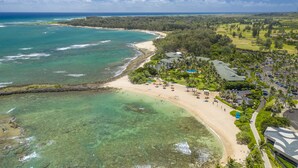 Vista aérea de un complejo turístico costero con playa, aguas cristalinas y vegetación exuberante.