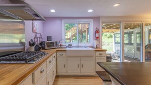 A kitchen with wooden countertops, a built-in stove, white cabinets, a window with a view of the outdoors, and a fire extinguisher on the wall. - Plum Creek - Large home with 2 kitchens close to Pier Cove! (Fennville)