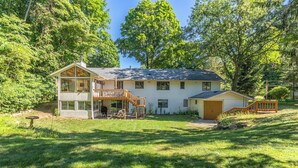 A two-story house with a covered porch, a small garage, and a wooden staircase leading to the upper level. - Plum Creek - Large home with 2 kitchens close to Pier Cove! (Fennville)