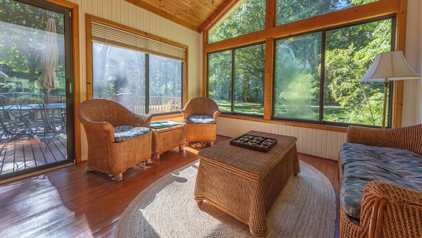 A spacious room with large windows, wicker furniture, and a view of a lush garden. - Plum Creek - Large home with 2 kitchens close to Pier Cove! (Fennville)