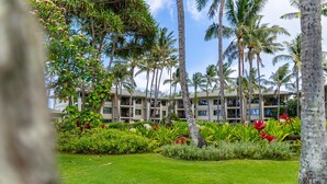 A hotel with a lush garden, palm trees, and a multi-story building with balconies. - Turtle Bay Villas 307 by Gather: Beachfront w/ Shared Pool/Spa/AC (Kahuku)